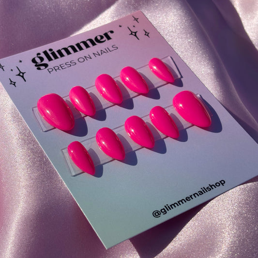 Set of pink press-on nails on a Glimmer branded card against a pink satin background