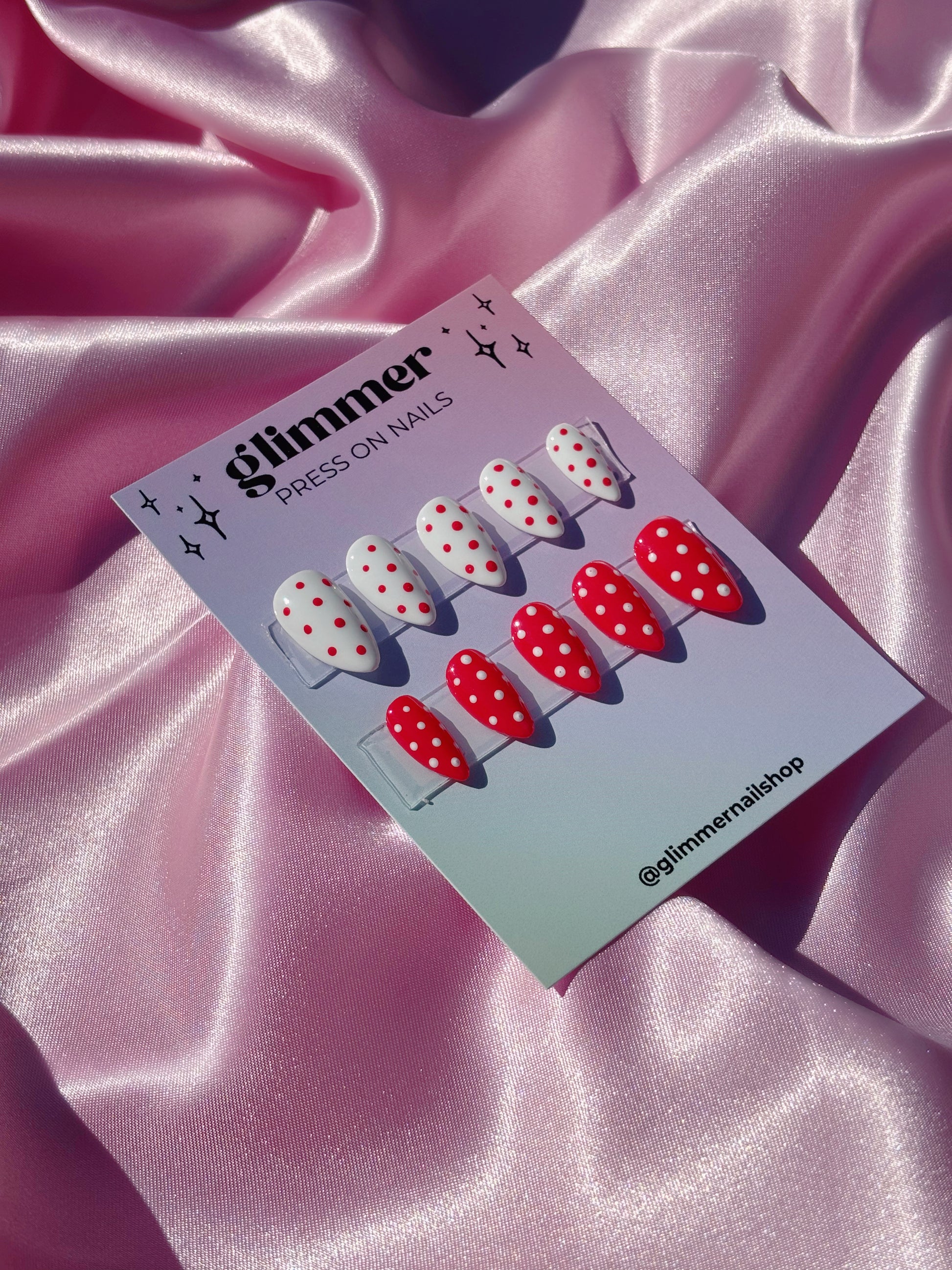 Card with red and white polka dot press-on nails on a pink satin background