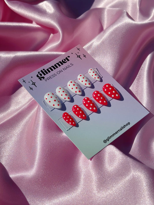 Card with red and white polka dot press-on nails on a pink satin background