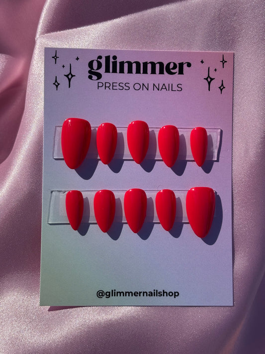 Red press-on nails on a card with 'Glimmer' branding on a pink satin background