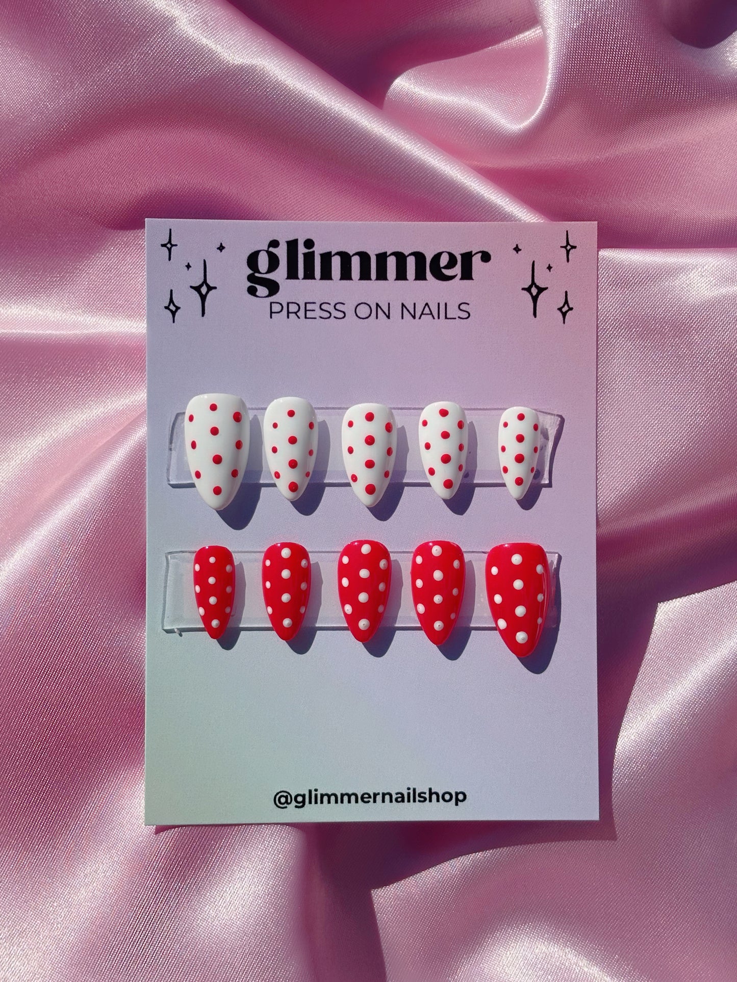 Packaging of 'glimmer' press on nails with red and white polka dot design on a pink fabric background.