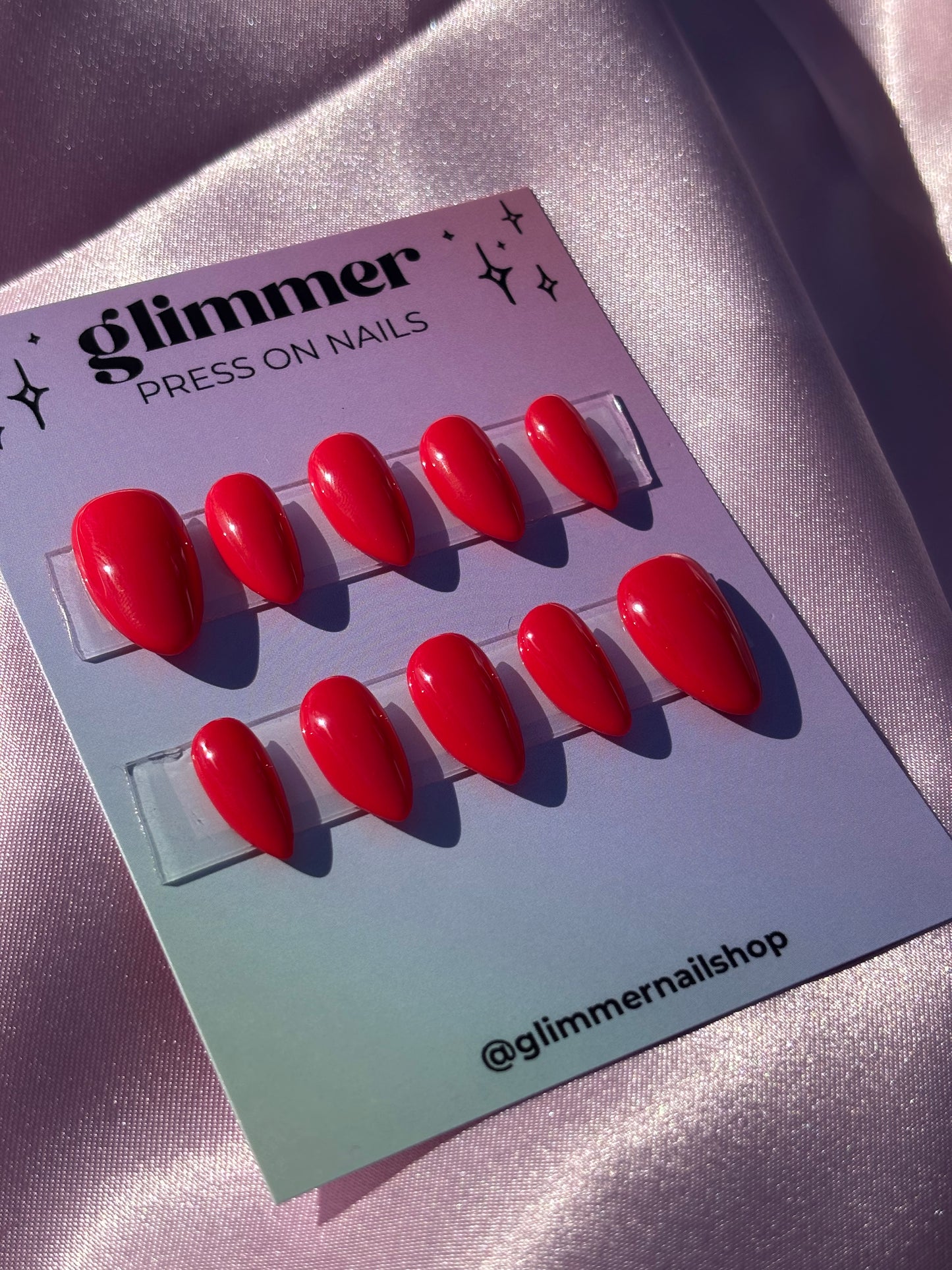 Red press-on nails on a Glimmer Nail Shop branded card against a metallic background