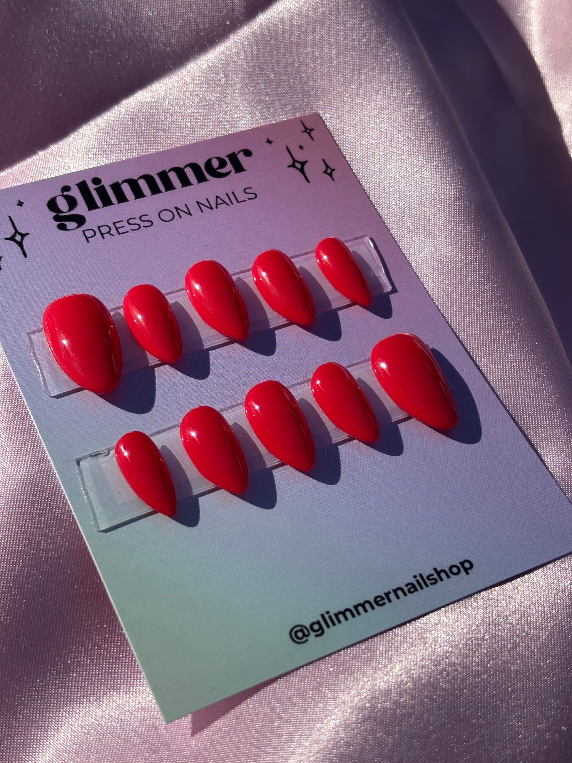 Red press-on nails on a Glimmer Nail Shop branded card against a metallic background