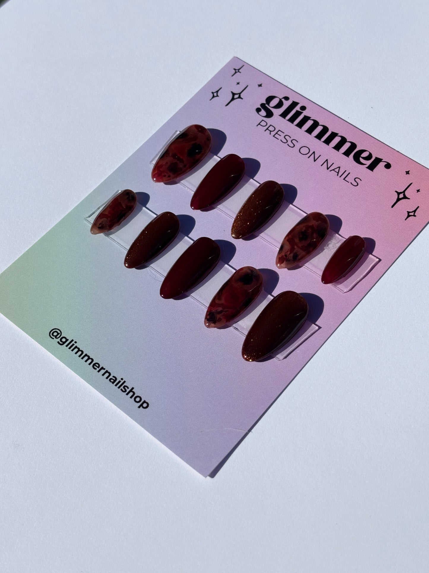 Glimmer press-on nails set in deep red shades, featuring glossy and marbled designs for stylish manicures.